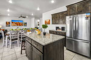 Kitchen with dark wood finish cabinetry, freestanding refrigerator, open floor plan, ceiling fan, and recessed lighting