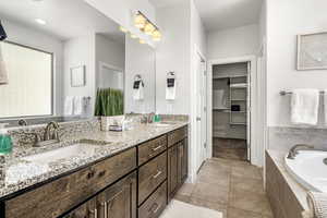 Bathroom featuring double vanity, a bath, a spacious closet, and light tile patterned flooring