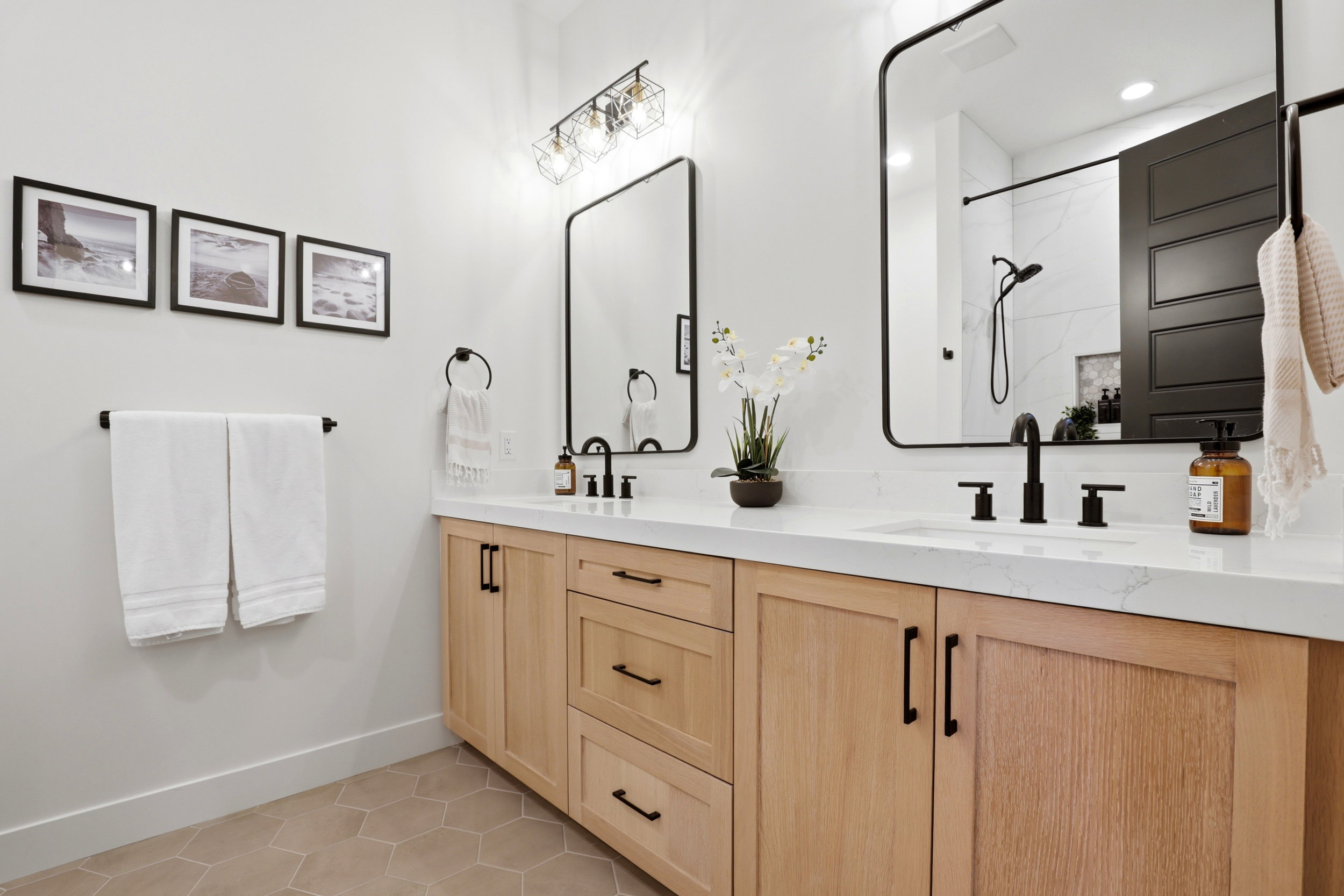 Dual vanity featuring light wood-finish cabinetry, white countertops, and matte black fixtures