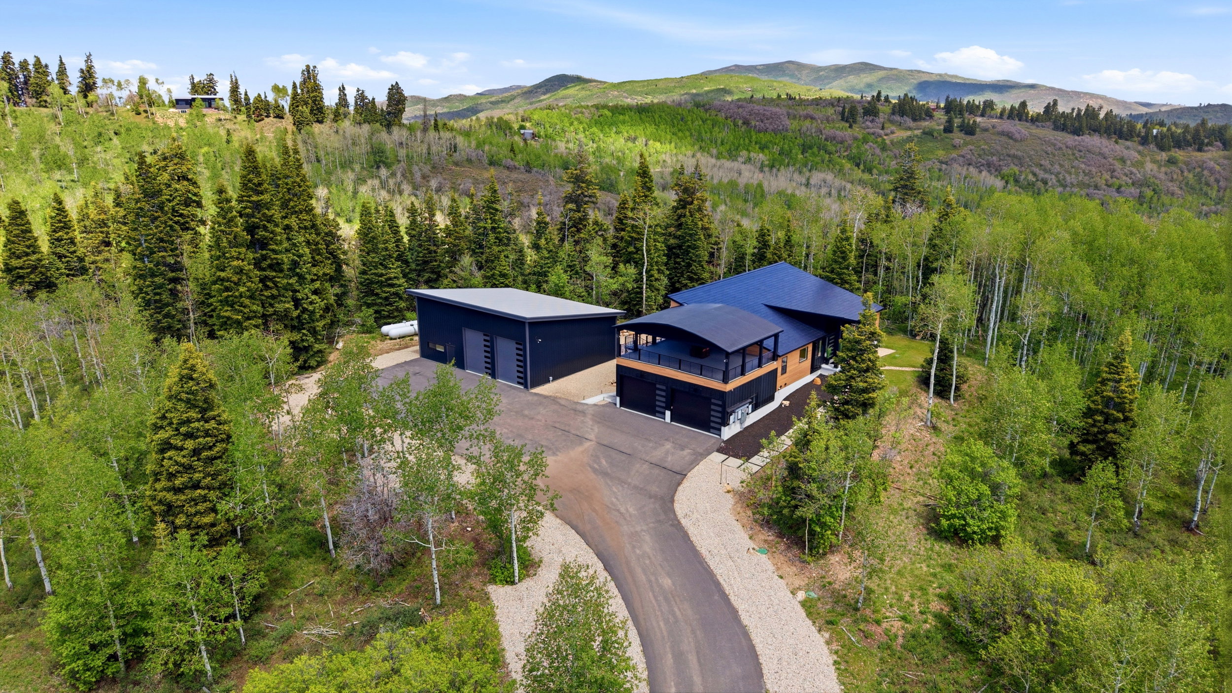 Contemporary residence featuring a dark-toned exterior with wood accents and a curved balcony, situated on a sloped lot