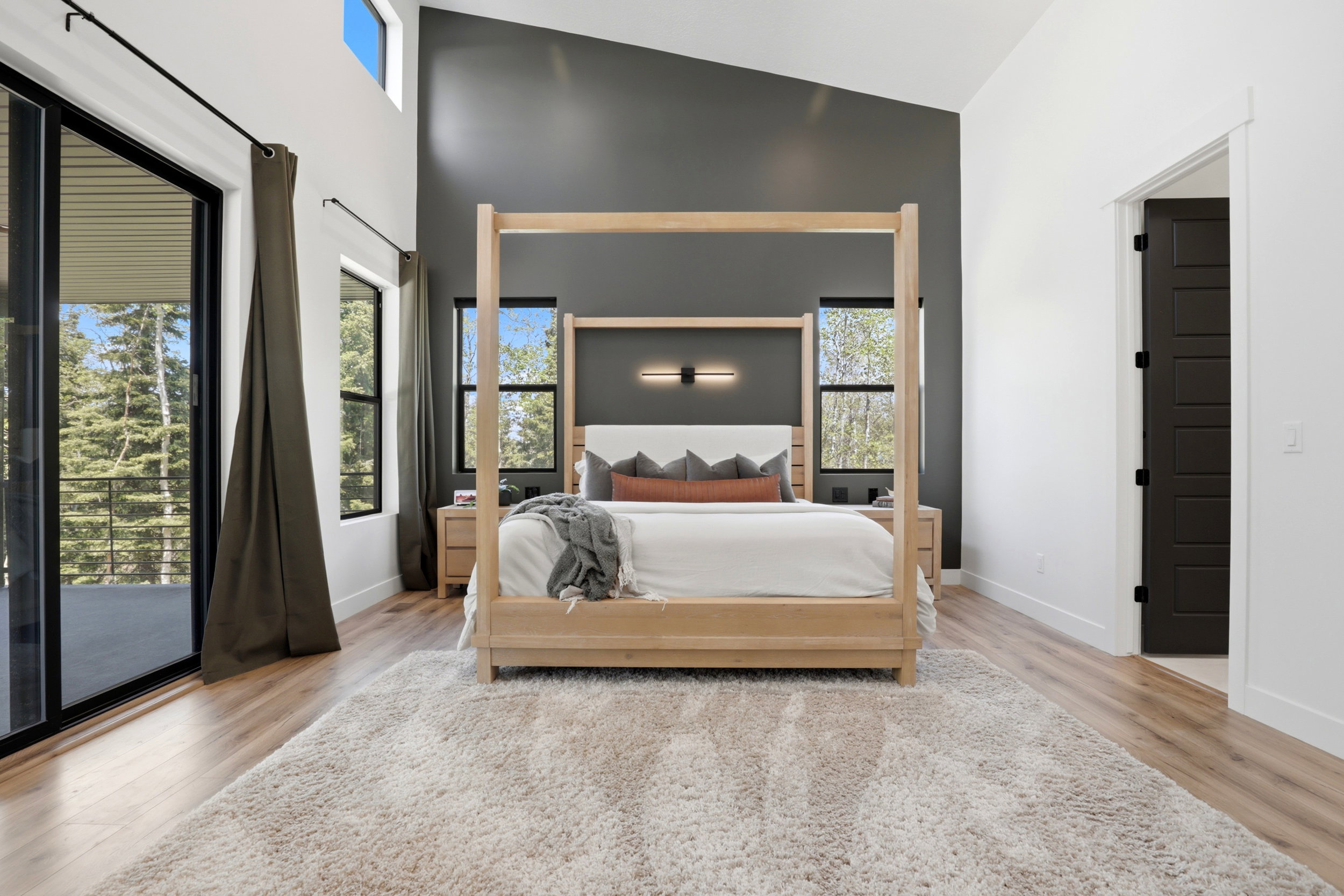 Vaulted ceiling bedroom with a dark accent wall, and a sliding glass door to an exterior balcony