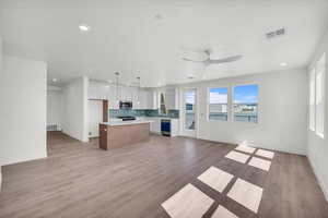 Kitchen featuring open floor plan, hanging light fixtures, a center island, light wood-type flooring, and two tone cabinets