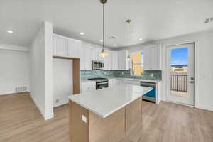 Dual tone kitchen with a kitchen island, light wood-type flooring, stainless steel appliances, pendant lighting, and two tone color scheme