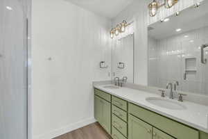 Full bath with double vanity, tiled shower, light wood-type flooring, and recessed lighting