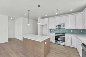Dual tone kitchen with stainless steel appliances, tasteful backsplash, light wood finished floors, a kitchen island, and two tone color scheme