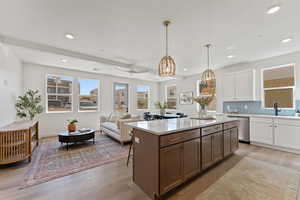 Kitchen with dual tone cabinetry, tasteful backsplash, a center island, light wood-type flooring, and decorative light fixtures