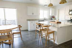 Kitchen featuring white cabinetry, hanging light fixtures, a kitchen breakfast bar, light stone countertops, and dark wood finished floors