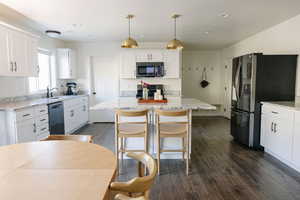 Kitchen featuring white cabinets, stainless steel appliances, pendant lighting, a kitchen island, and dark wood-style flooring