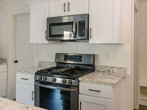 Kitchen featuring stainless steel appliances, white cabinetry, light stone counters, and dark wood finished floors