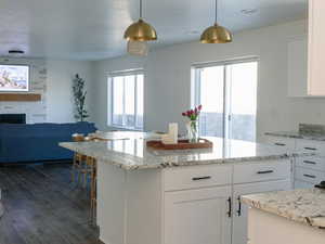 Kitchen with white cabinets, decorative light fixtures, light stone countertops, and dark wood-type flooring