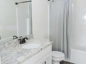 Full bath featuring shower / tub combo with curtain, vanity, and dark wood-style flooring