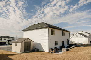 Back of house with a patio area, a shed, roof with shingles, and a yard