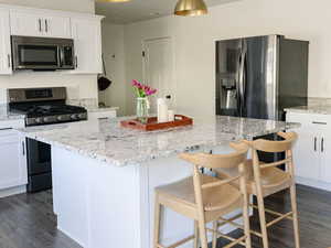 Kitchen with stainless steel appliances, white cabinetry, decorative light fixtures, light stone countertops, and dark wood-style floors