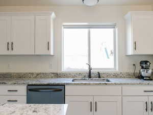 Kitchen with white cabinetry, light stone counters, and dishwasher