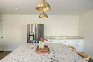 Kitchen featuring stainless steel fridge, light stone counters, white cabinets, and a breakfast bar area