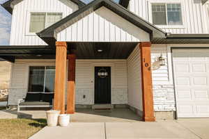 Entrance to property with covered porch, a garage, board and batten siding, and stone siding