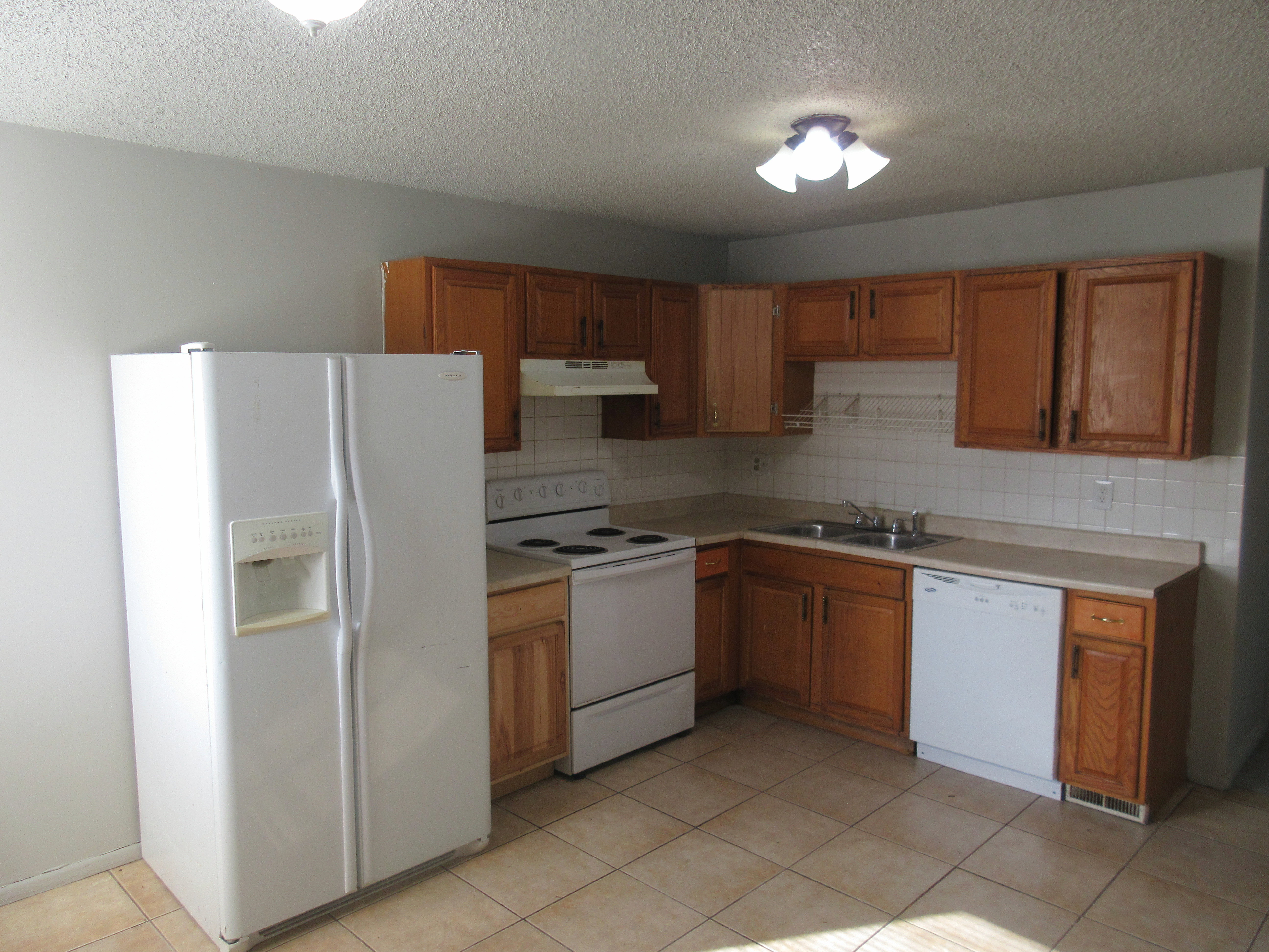 Kitchen featuring white appliances, wood finish cabinetry, light countertops, a textured ceiling, and backsplash