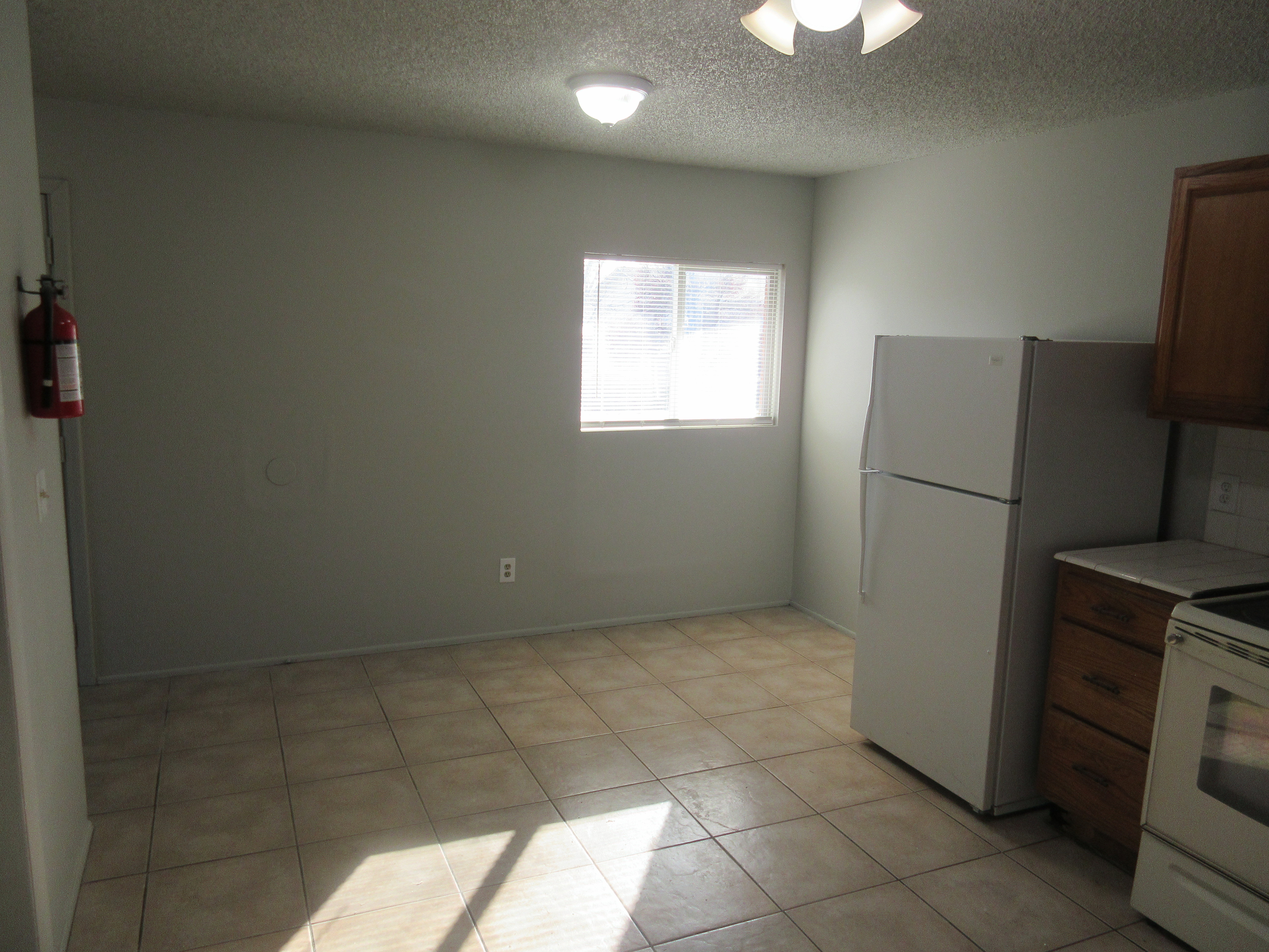 Kitchen with white appliances, a textured ceiling, wood finish cabinets, light countertops, and light tile patterned flooring