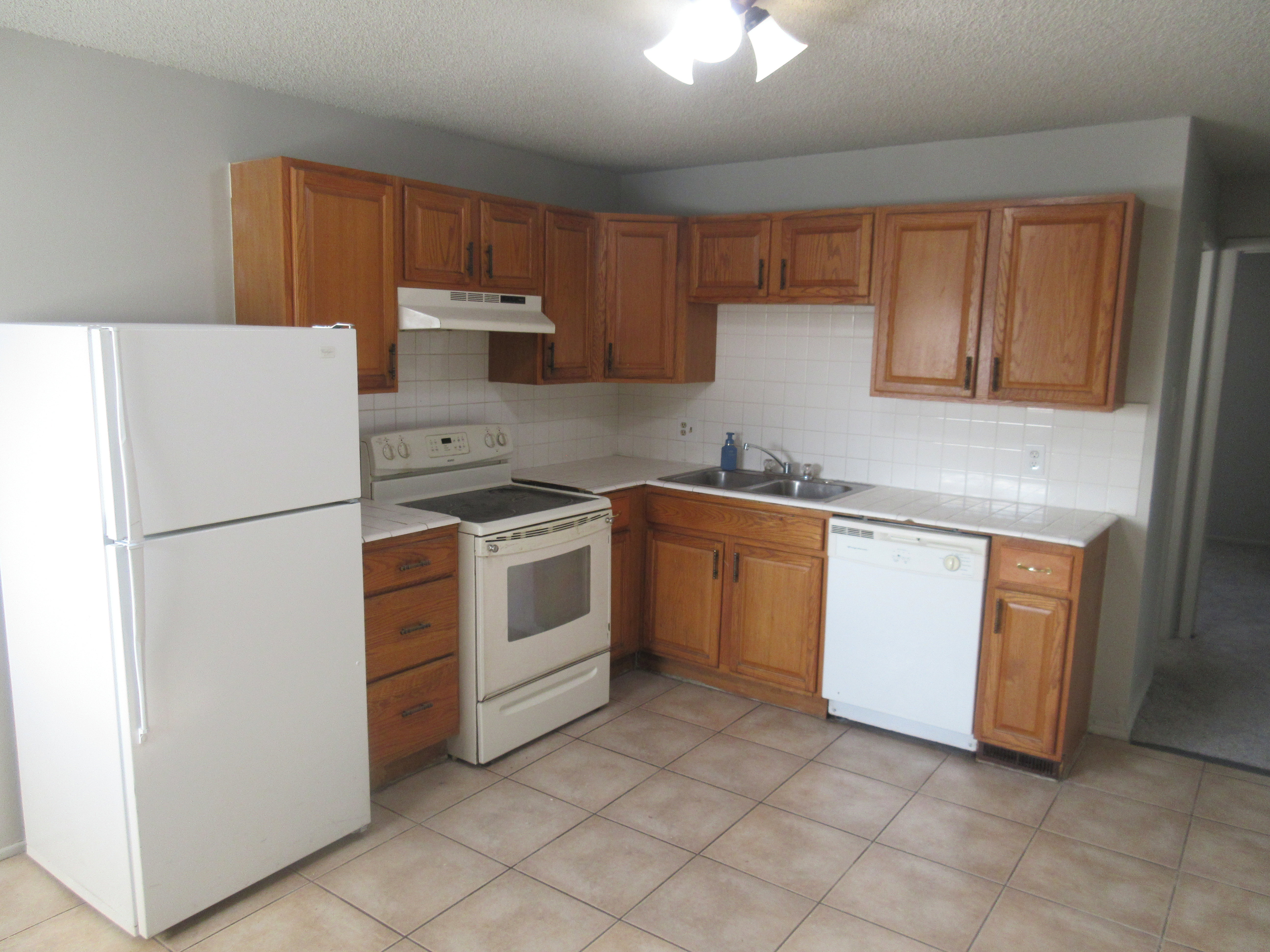 Kitchen with white appliances, wood finish cabinetry, a textured ceiling, backsplash, and light tile patterned floors