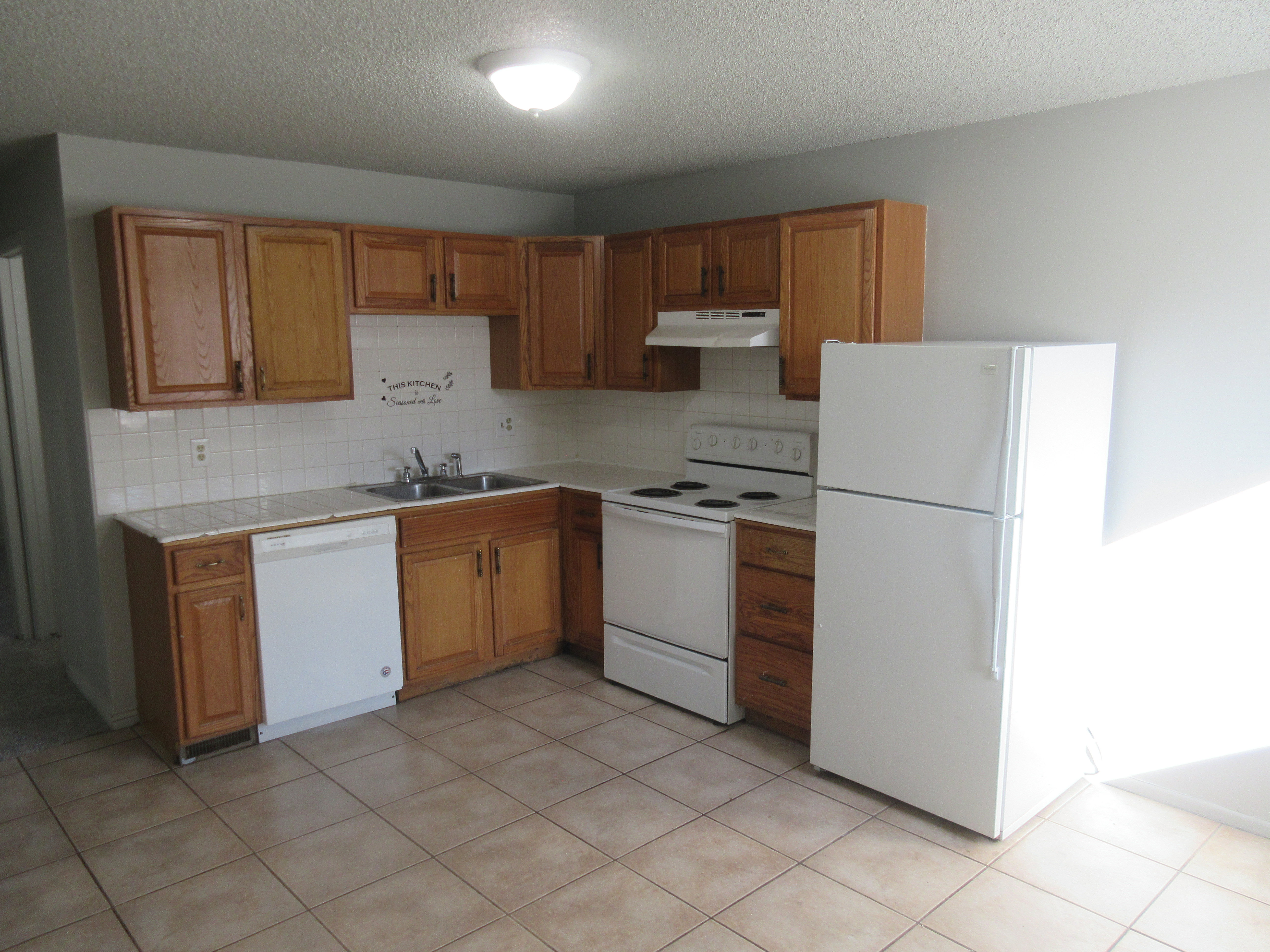 Kitchen featuring white appliances, a textured ceiling, wood finish cabinets, decorative backsplash, and tile countertops