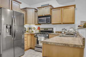 Kitchen featuring stainless steel appliances, light countertops, a peninsula, light tile patterned flooring, and light wood finish cabinets