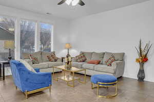 Tiled living room with a ceiling fan and baseboards