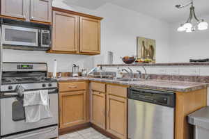 Kitchen with stainless steel appliances, a peninsula, suspended lighting, light tile patterned floors, and light countertops