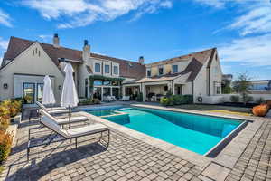 Rear view of property with a patio, a pool with connected hot tub, stucco siding, and a chimney