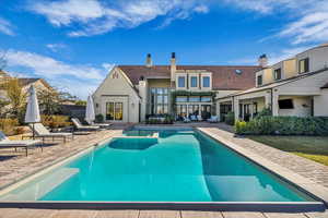 Back of property featuring a patio, a chimney, a pool with connected hot tub, and stucco siding
