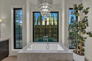Full bath with a bath, vanity, a chandelier, and light wood-style flooring