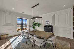 Dining area with dark wood-type flooring, a decorative wall, recessed lighting, and crown molding