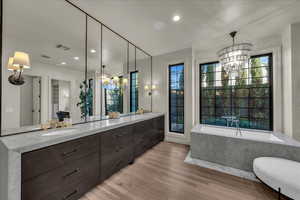 Full bathroom featuring suspended lighting, double vanity, light wood-style flooring, and a freestanding tub