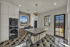 Kitchen with stacked washer and clothes dryer, a center island, hanging light fixtures, a kitchen breakfast bar, and dual tone cabinets