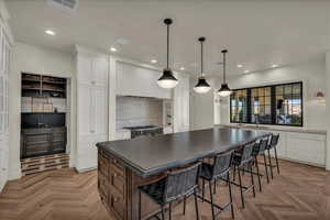 Kitchen featuring two tone cabinets, a kitchen bar, hanging light fixtures, parquet flooring, and a center island