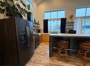 Kitchen with black appliances, a breakfast bar, light wood-type flooring, decorative backsplash, and lofted ceiling