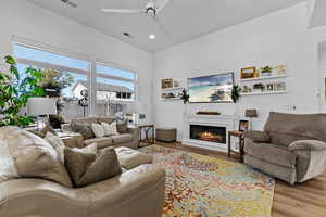 Living room featuring ceiling fan, a glass covered fireplace, recessed lighting, and wood finished floors