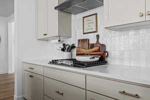 Kitchen featuring extractor fan, light stone counters, tasteful backsplash, white cabinetry, and stainless steel gas stovetop