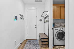 Laundry area featuring washer / dryer, cabinet space, and light wood-style flooring