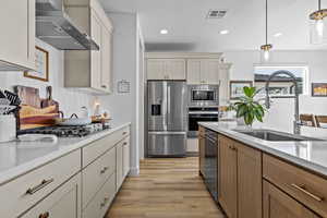 Kitchen featuring stainless steel appliances, decorative light fixtures, light wood-type flooring, tasteful backsplash, and light stone counters