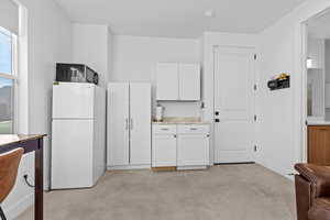 Kitchen featuring freestanding refrigerator, light countertops, white cabinetry, and light colored carpet
