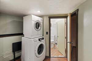 Laundry room with a textured ceiling, stacked washer and clothes dryer, and wood finished floors