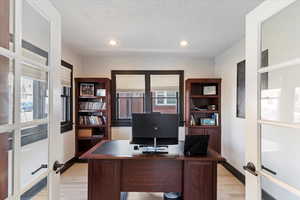 Home office featuring french doors, light wood-style flooring, a textured ceiling, and recessed lighting