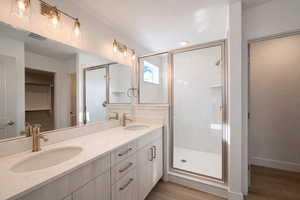 Bathroom featuring double vanity, a marble finish shower, a walk in closet, and light wood-style floors