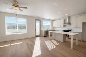 Kitchen with stainless steel appliances, light wood-style flooring, decorative backsplash, a ceiling fan, and a kitchen island