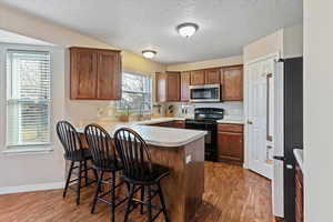 Kitchen with black range with electric cooktop, light countertops, freestanding refrigerator, dark wood-style flooring, and a peninsula