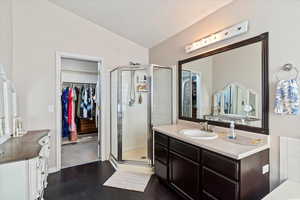 Full bath featuring a spacious closet, vanity, a shower stall, and dark wood-style floors
