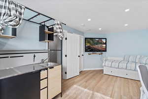 Kitchen with stainless steel countertops, open shelves, light wood-type flooring, light wood finish cabinets, and recessed lighting