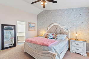 Bedroom with wallpapered walls, an accent wall, lofted ceiling, connected bathroom, and a ceiling fan