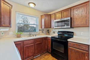 Kitchen with black range with electric cooktop, stainless steel microwave, light countertops, a textured ceiling, and light wood-type flooring