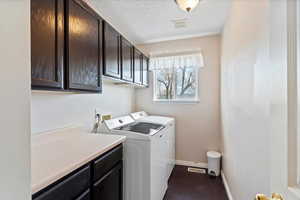 Laundry area with cabinet space, a textured ceiling, washer and dryer, and dark wood-style floors